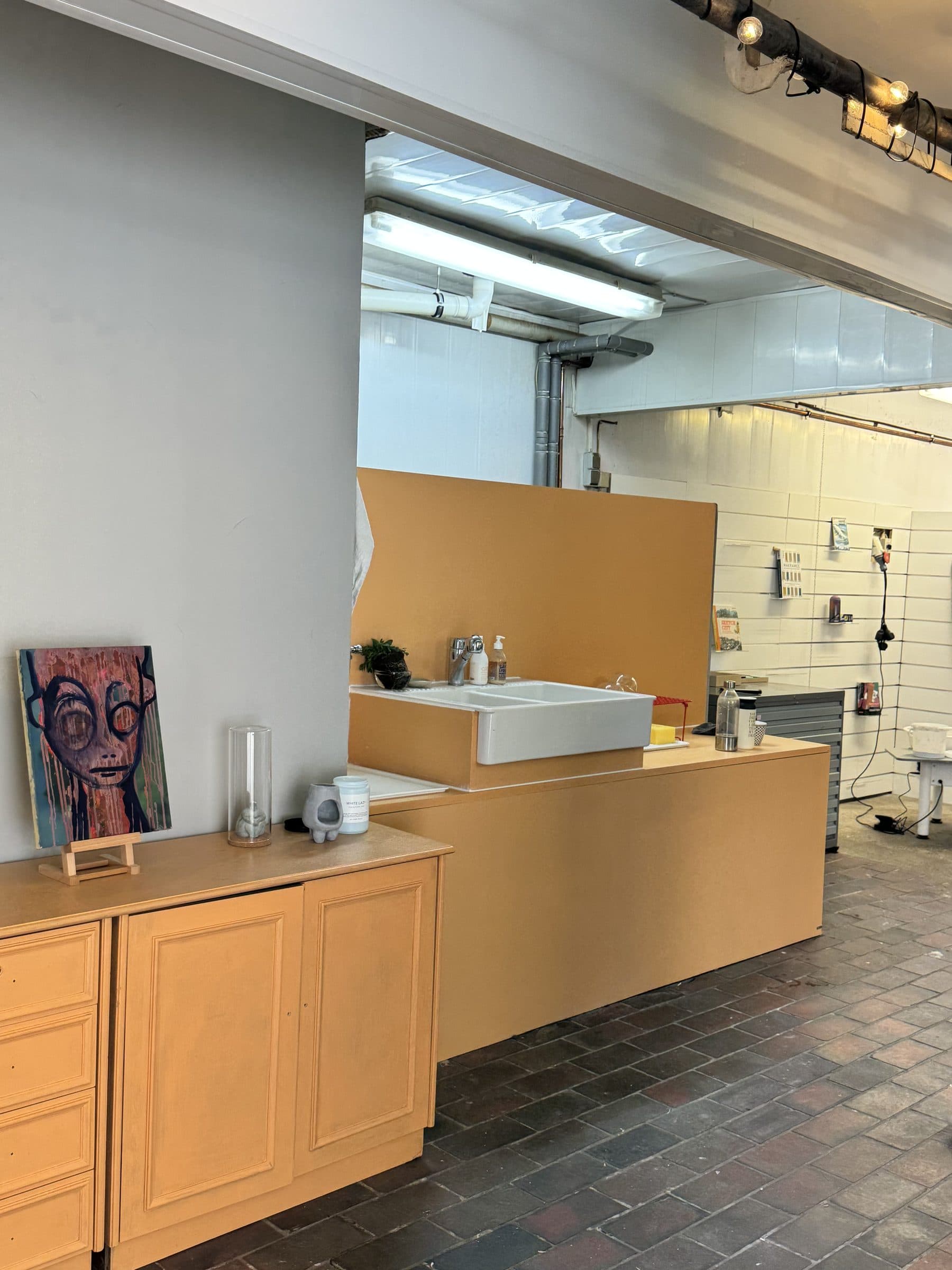 Blick in den Atelierraum mit Waschbecken, Holzkommode und Bild auf der Staffelei